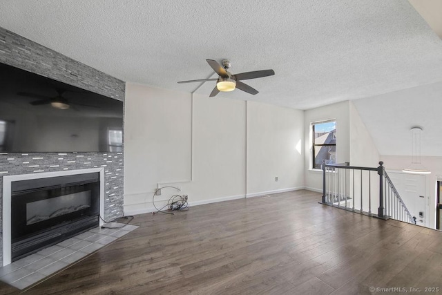 unfurnished living room featuring a ceiling fan, a tile fireplace, a textured ceiling, and wood finished floors