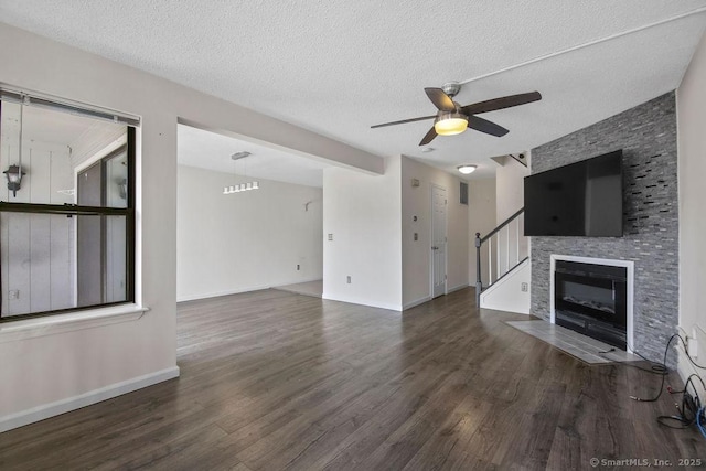 unfurnished living room with a textured ceiling, wood finished floors, a fireplace with flush hearth, a ceiling fan, and baseboards