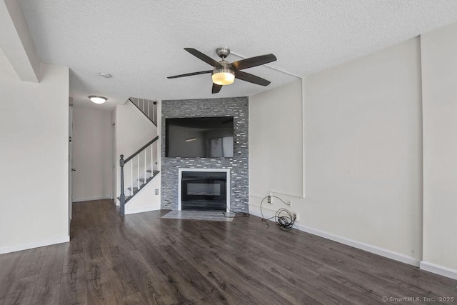 unfurnished living room featuring a large fireplace, a textured ceiling, wood finished floors, baseboards, and stairs