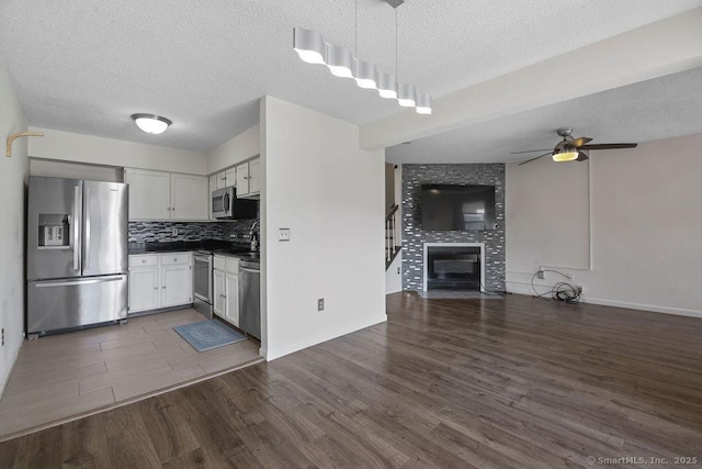 kitchen featuring open floor plan, appliances with stainless steel finishes, backsplash, dark countertops, and dark wood finished floors