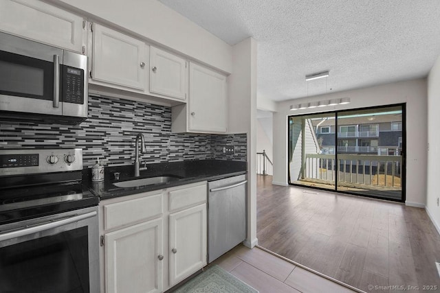 kitchen with dark countertops, backsplash, light wood-style flooring, appliances with stainless steel finishes, and a sink