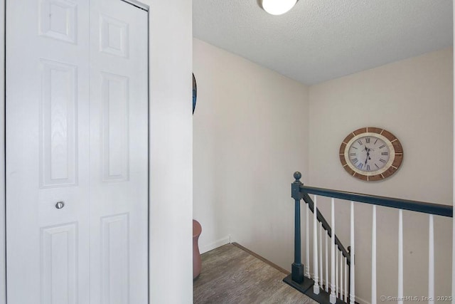 corridor featuring baseboards, a textured ceiling, an upstairs landing, and wood finished floors