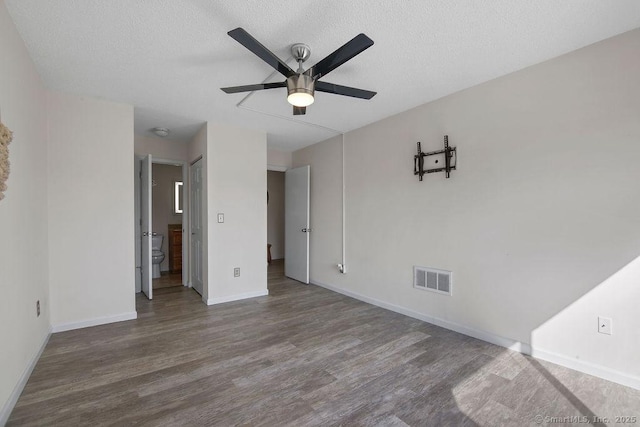 spare room with a textured ceiling, wood finished floors, a ceiling fan, visible vents, and baseboards