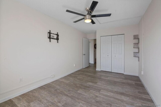 unfurnished bedroom featuring a ceiling fan, a closet, baseboards, and wood finished floors