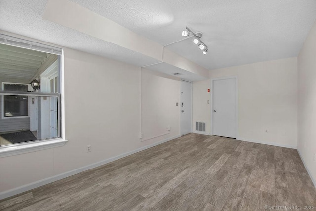 empty room with baseboards, a textured ceiling, visible vents, and wood finished floors