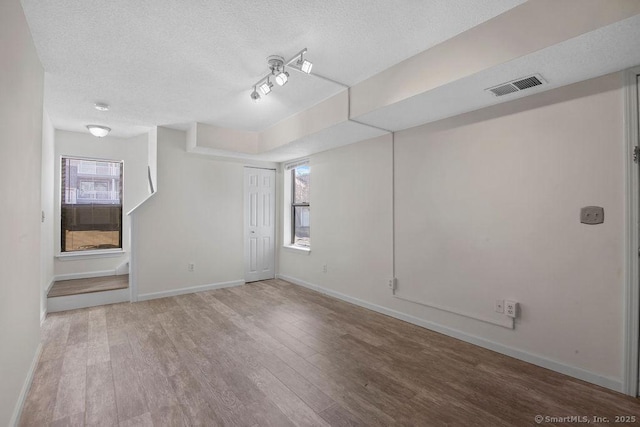 spare room with a textured ceiling, wood finished floors, visible vents, baseboards, and track lighting