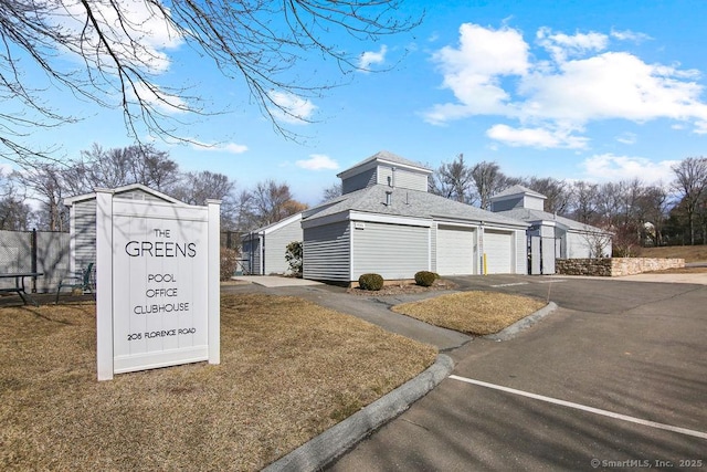 view of property exterior with a garage, a shingled roof, driveway, and an outdoor structure