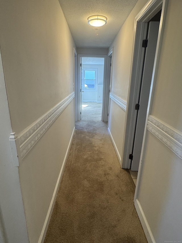 corridor with a textured ceiling, baseboards, and light colored carpet