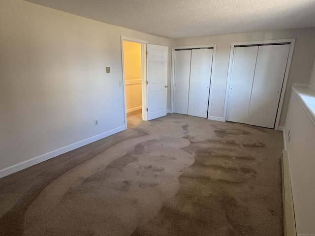 unfurnished bedroom featuring carpet floors, a textured ceiling, baseboards, and two closets