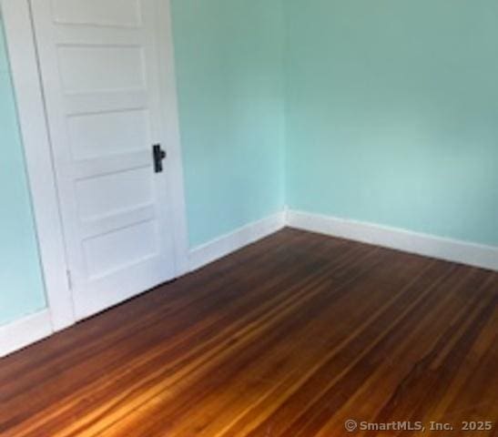 unfurnished room with baseboards and dark wood-type flooring