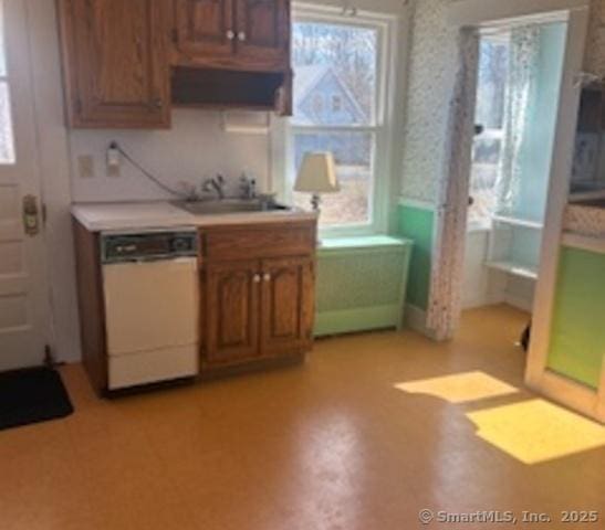 kitchen with a sink, brown cabinetry, wallpapered walls, dishwasher, and light countertops