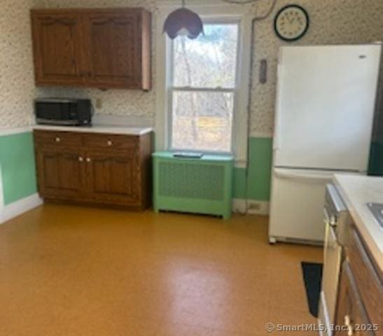 kitchen with stainless steel microwave, light countertops, freestanding refrigerator, and wallpapered walls