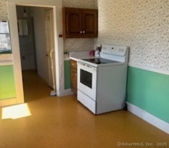 kitchen featuring light floors, a wainscoted wall, wallpapered walls, light countertops, and white electric range