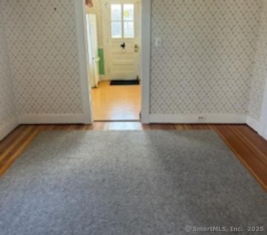 spare room featuring wallpapered walls, wood finished floors, and baseboards