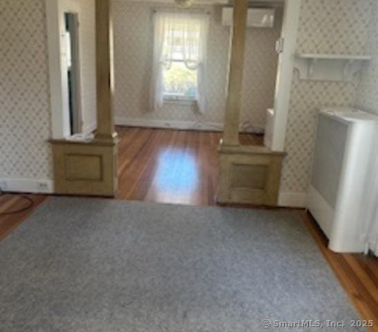 unfurnished living room with wallpapered walls, radiator heating unit, and wood finished floors