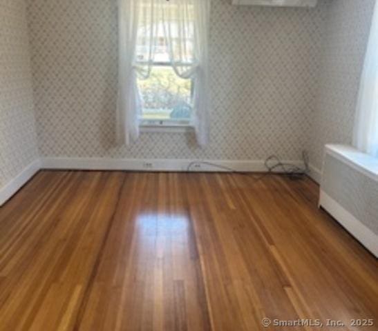 empty room with wallpapered walls, baseboards, and wood finished floors