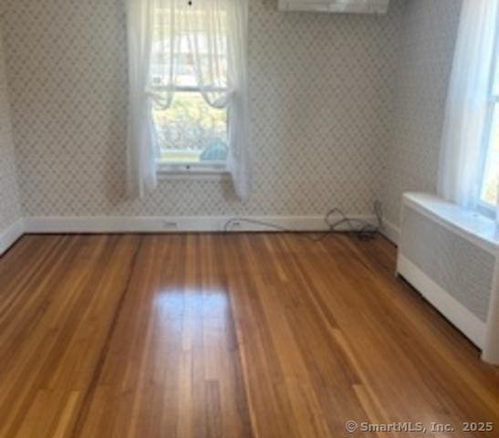 empty room with baseboards, wood finished floors, radiator heating unit, and wallpapered walls