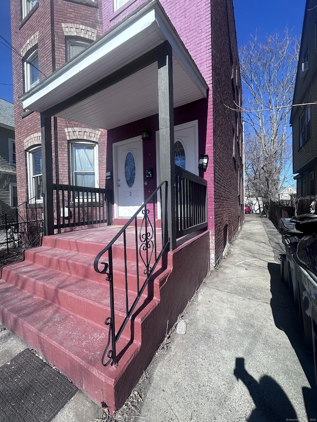 entrance to property featuring covered porch and brick siding