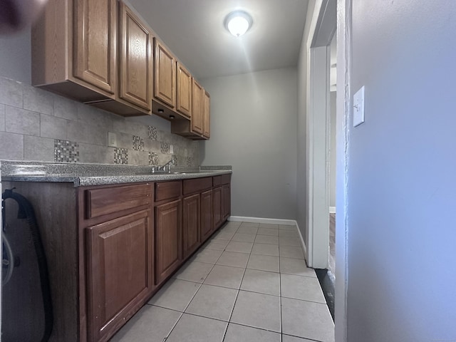 kitchen with light tile patterned floors, a sink, backsplash, and baseboards