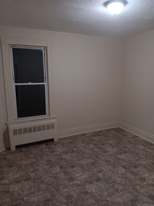 spare room featuring radiator, a textured ceiling, and baseboards