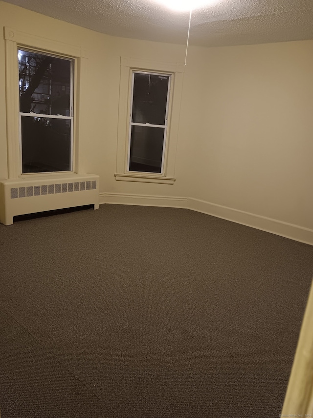 carpeted spare room featuring radiator, a textured ceiling, and baseboards