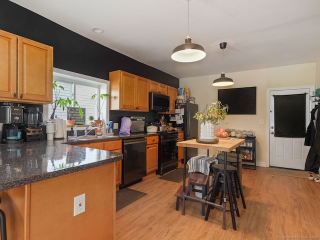 kitchen featuring a sink, baseboards, hanging light fixtures, light wood-type flooring, and black appliances