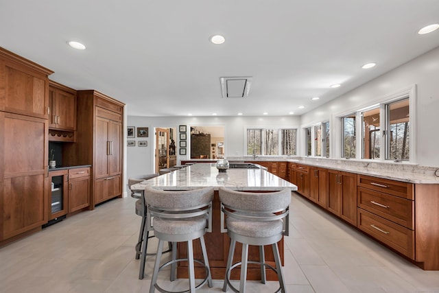 kitchen with a kitchen bar, a large island, light stone countertops, and brown cabinets