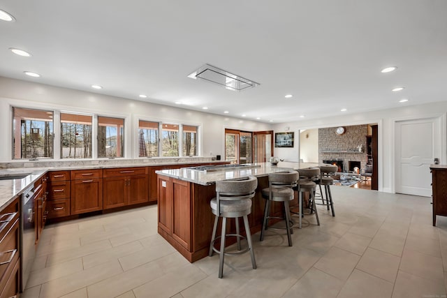 kitchen with a kitchen bar, brown cabinets, light stone counters, stainless steel appliances, and a brick fireplace