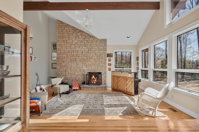 interior space with wood finished floors, high vaulted ceiling, beamed ceiling, a large fireplace, and a chandelier