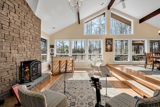 living area with beamed ceiling, high vaulted ceiling, a notable chandelier, wood finished floors, and a stone fireplace