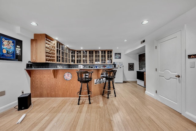 kitchen featuring freestanding refrigerator, a breakfast bar area, glass insert cabinets, and light wood finished floors