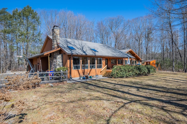 view of front of home featuring stone siding, a chimney, a front yard, and roof with shingles