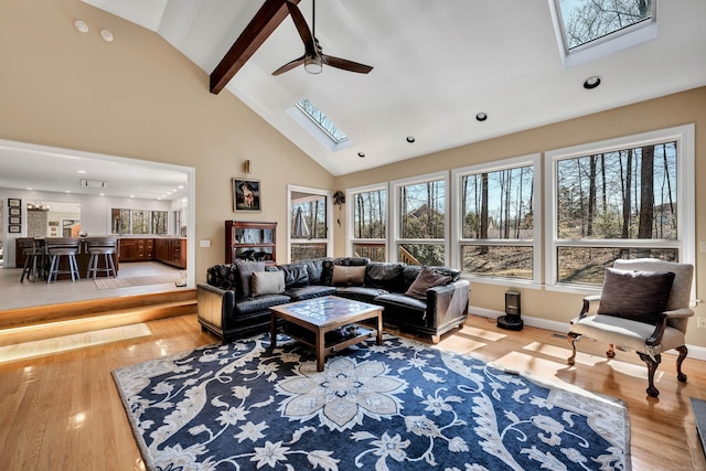 living area featuring baseboards, beamed ceiling, a skylight, wood finished floors, and high vaulted ceiling