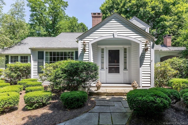 doorway to property with roof with shingles and a chimney