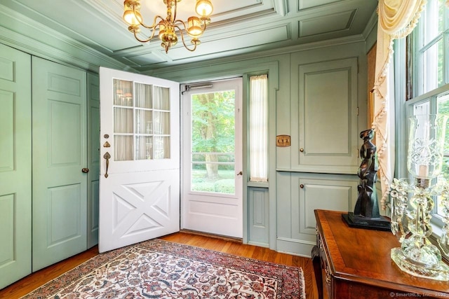 doorway to outside featuring light wood finished floors, a decorative wall, an inviting chandelier, and crown molding