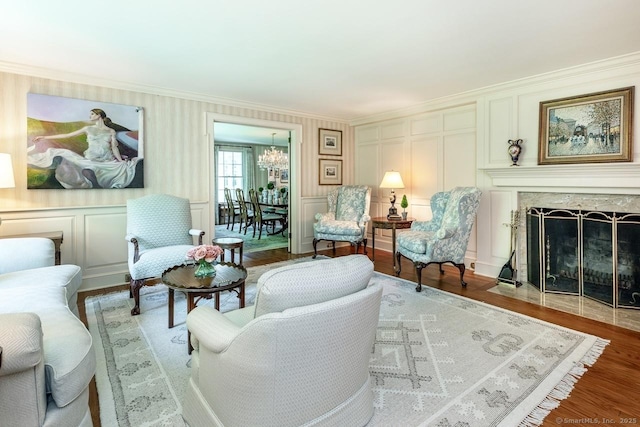 living area featuring wood finished floors, crown molding, a stone fireplace, a chandelier, and a decorative wall