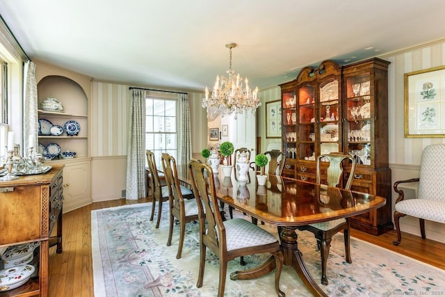 dining room featuring ornamental molding, wallpapered walls, light wood finished floors, and a notable chandelier