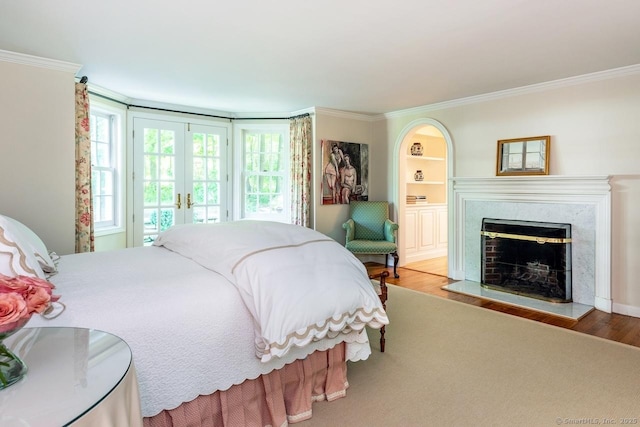 bedroom with french doors, ornamental molding, wood finished floors, and a high end fireplace