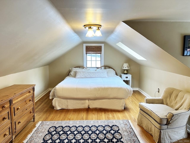 bedroom with lofted ceiling with skylight, baseboards, and wood finished floors