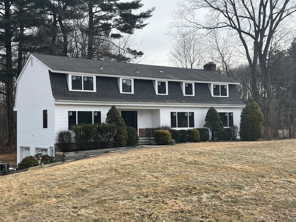 colonial inspired home with a shingled roof, an attached garage, a gambrel roof, central AC unit, and a front lawn