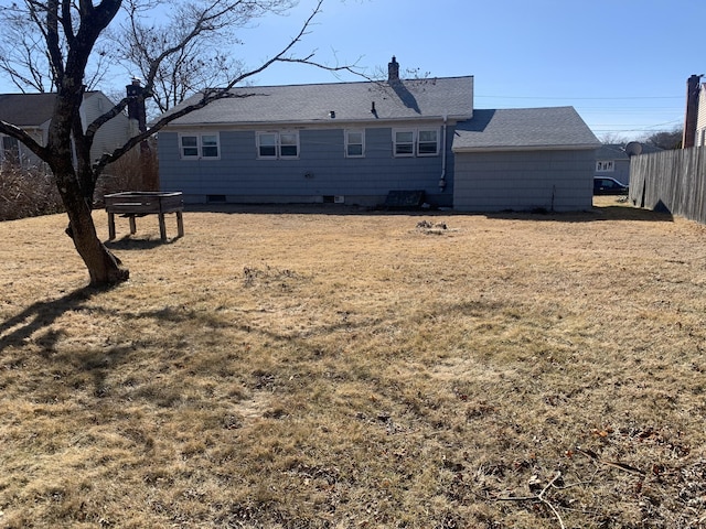 back of house featuring roof with shingles, a chimney, fence, and a lawn