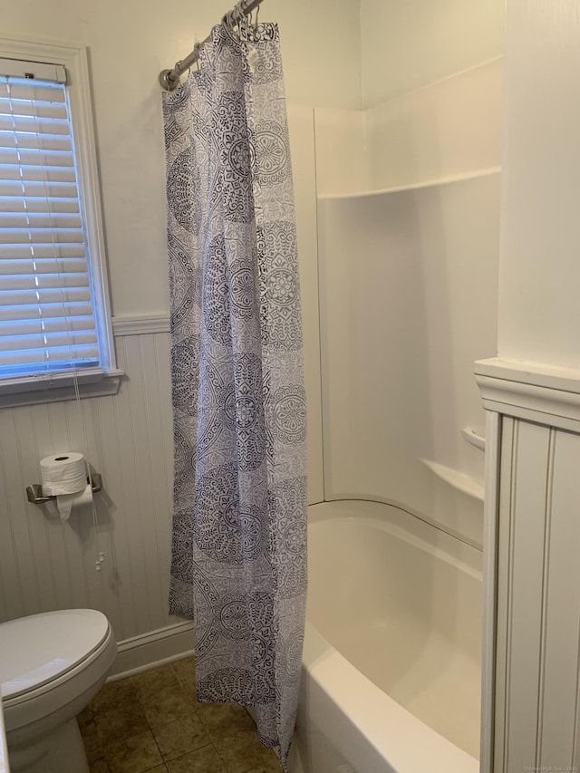 full bathroom with shower / tub combo, wainscoting, toilet, and tile patterned floors