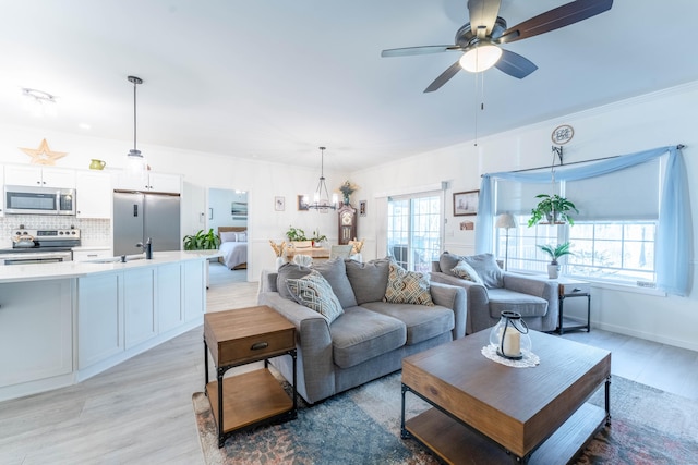 living area with light wood-style floors, baseboards, and ceiling fan with notable chandelier