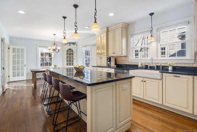 kitchen with a breakfast bar area, a sink, cream cabinetry, decorative backsplash, and dark wood-style floors