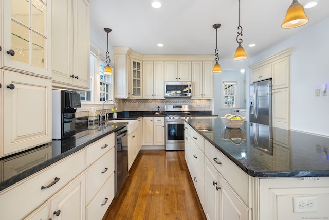 kitchen featuring dark wood finished floors, decorative backsplash, appliances with stainless steel finishes, cream cabinetry, and a sink