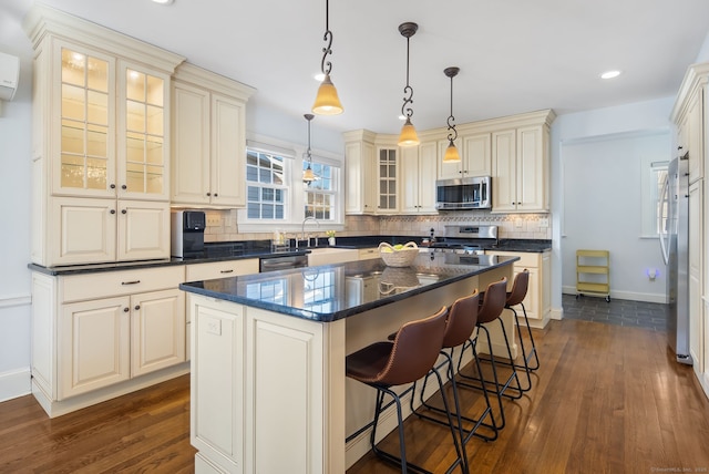 kitchen with stainless steel appliances, a kitchen island, backsplash, a kitchen bar, and pendant lighting