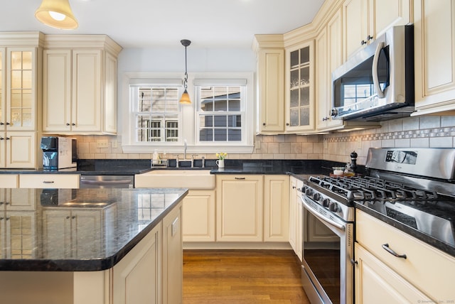 kitchen with stainless steel appliances, hanging light fixtures, cream cabinets, a sink, and wood finished floors