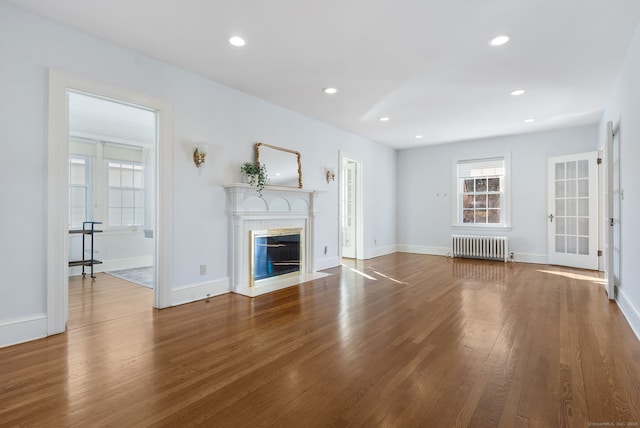 unfurnished living room with a fireplace with flush hearth, recessed lighting, radiator, and wood finished floors