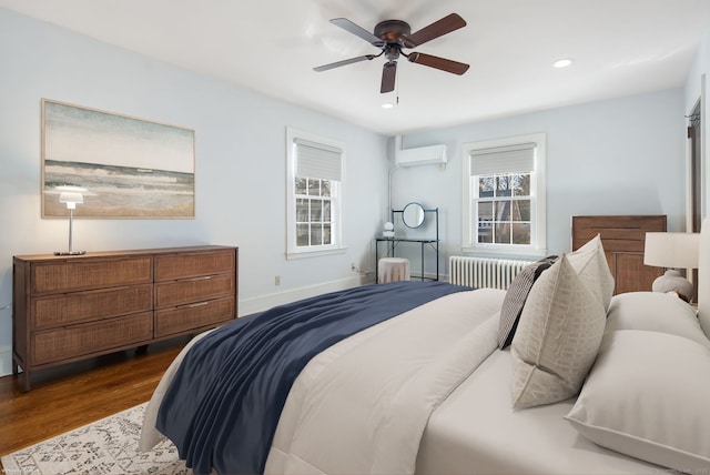 bedroom featuring radiator heating unit, multiple windows, an AC wall unit, and wood finished floors