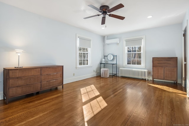 bedroom featuring radiator, a wall unit AC, wood finished floors, and multiple windows